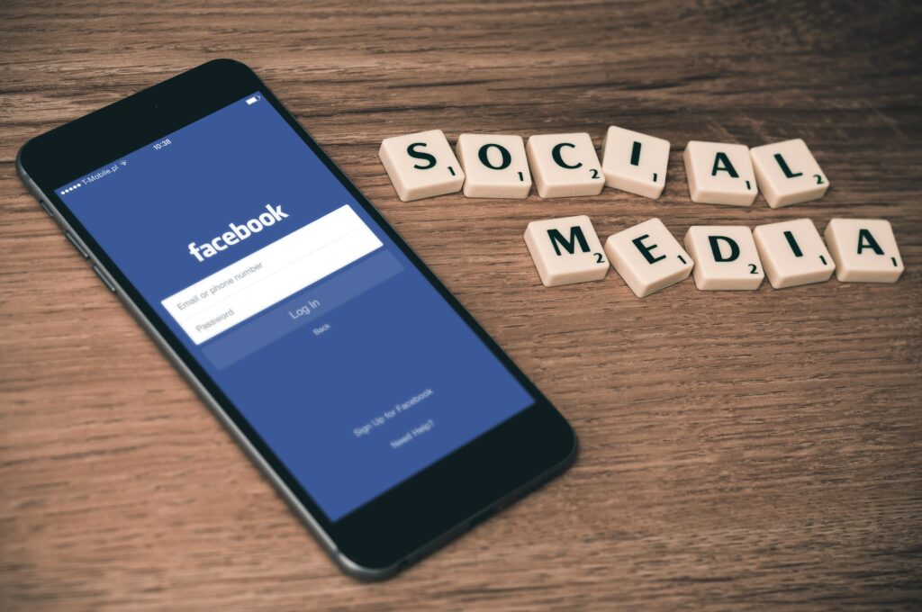 Smartphone mit Facebook App , daneben steht SOCIAL MEDIA Plattformen